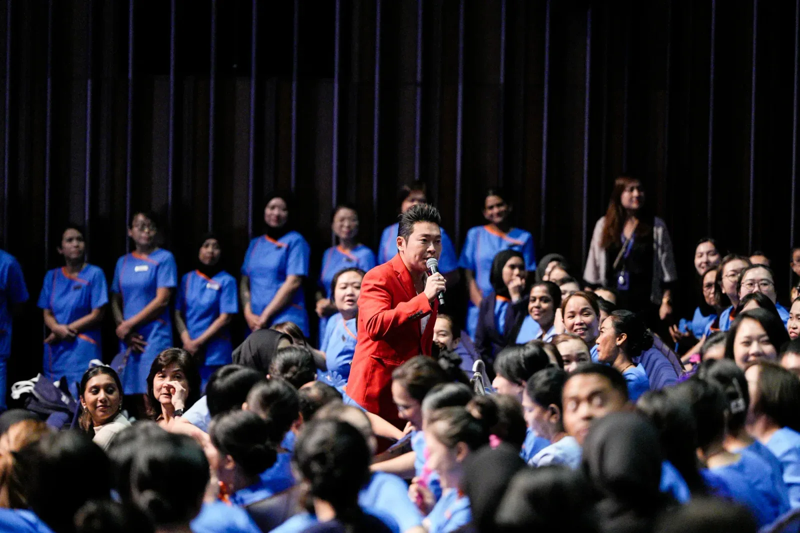 James Yang on stage in front of a full auditorium at NUHS Superstar Nurses 2024